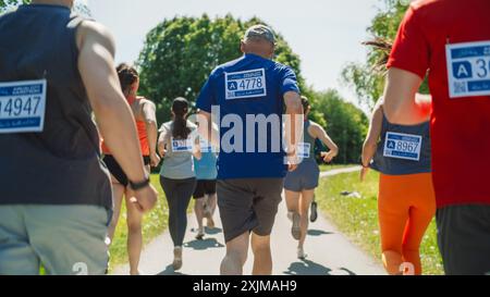 Rückansicht: Porträt einer vielfältigen Gruppe von Menschen, die an einem Marathon teilnehmen und durch einen Park Trail laufen. Aktiver Seniorenmann im Wettbewerb mit jungen Joggern, gesund bleiben Stockfoto