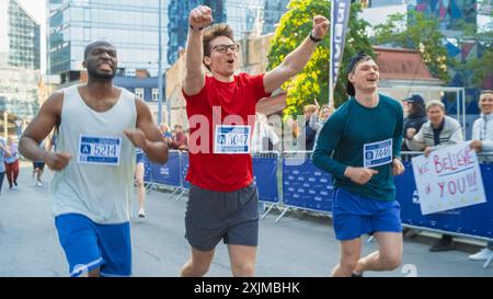 Happy Young Male feiert und hebt die Hände beim Überqueren der Ziellinie in einem Rennen. Porträt einer lächelnden Gruppe von Menschen, die an einem City Marathon teilnehmen Stockfoto