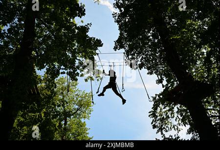 PRODUKTION - 19. Juli 2024, Hessen, Wiesbaden: Eine junge Frau zielt hoch im Kletterwald Neroberg. Der Kletterpark für junge und erfahrene Freizeitsportler liegt auf Wiesbadens Hausberg, umgeben von Buchen und Eichen. Der höchste Punkt ist ein Abenteuernest in einer Höhe von 25 Metern. Foto: Arne Dedert/dpa Stockfoto