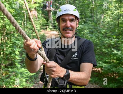 PRODUKTION - 19. Juli 2024, Hessen, Wiesbaden: Thorsten Held, Geschäftsführer von Kletterwald Neroberg, hält sich an einem Seil auf einem Kurs fest. Der Kletterpark für junge und erfahrene Freizeitsportler liegt auf Wiesbadens Hausberg, umgeben von Buchen und Eichen. Der höchste Punkt ist ein Abenteuernest in einer Höhe von 25 Metern. Foto: Arne Dedert/dpa Stockfoto