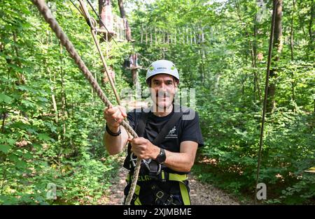 PRODUKTION - 19. Juli 2024, Hessen, Wiesbaden: Thorsten Held, Geschäftsführer von Kletterwald Neroberg, hält sich an einem Seil auf einem Kurs fest. Der Kletterpark für junge und erfahrene Freizeitsportler liegt auf Wiesbadens Hausberg, umgeben von Buchen und Eichen. Der höchste Punkt ist ein Abenteuernest in einer Höhe von 25 Metern. Foto: Arne Dedert/dpa Stockfoto