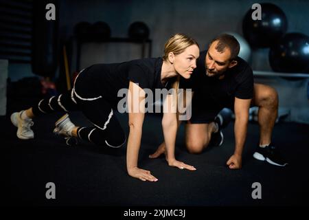Junge Sportlerin, die Liegestütze während des Trainingskurses mit einem Trainer im Health Club macht. Stockfoto