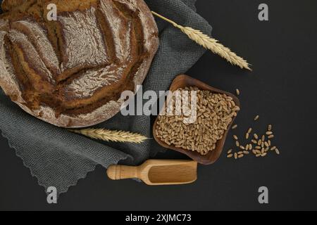 Brotlaib und Weizenkorn auf einem grauen Küchentuch auf einer schwarzen Tafel, Draufsicht mit Platz zum Kopieren Stockfoto