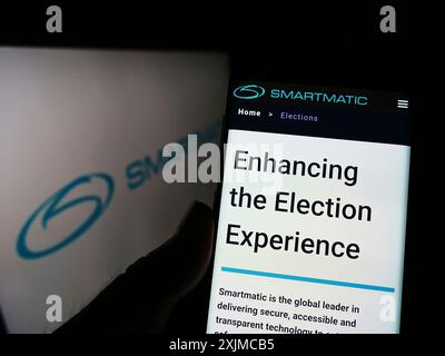 Stuttgart, 21.05.2022: Person, die ein Mobiltelefon hält, mit Webseite der Wahlsystemgesellschaft Smartmatic Corporation auf dem Bildschirm vor dem Logo. Stockfoto
