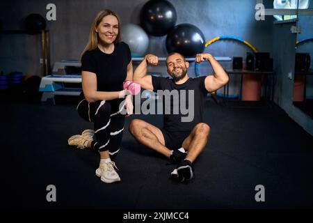 Glückliches, athletisches Paar, das nach hartem Training in einem Fitnessstudio ihre Muskeln beugt und die Kamera ansieht und lächelt. Stockfoto