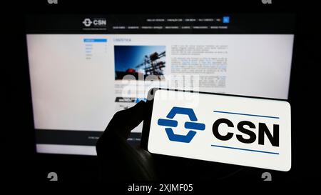 Stuttgart, Deutschland, 06.12.2022: Person mit Mobiltelefon mit Logo der Firma Companhia Siderurgica Nacional (CSN) auf dem Bildschirm vor dem Geschäft Stockfoto