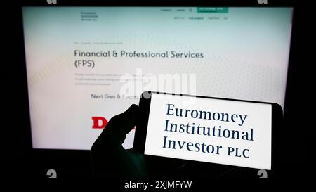 Stuttgart, Deutschland, 07.03.2022: Person, die ein Mobiltelefon mit dem Logo der Firma Euromoney Institutional Investor plc vor dem Unternehmen hält Stockfoto