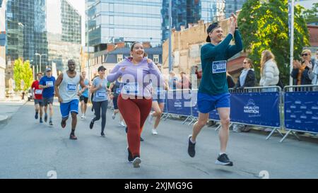 Porträt einer lächelnden Läuferin in Übergröße, die die Ziellinie überquert und ihre Willenskraft demonstriert. Die Teilnehmer des Friendly City Marathons winken dem Publikum zu Stockfoto