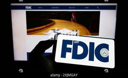 Stuttgart, Deutschland, 10.07.2022: Person mit Mobiltelefon mit Logo der US Federal Deposit Insurance Corporation (FDIC) auf dem Bildschirm vor der Webseite. Stockfoto