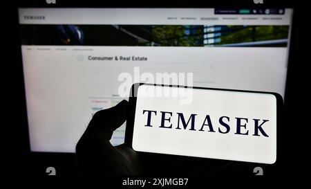 Stuttgart, 15.07.2022: Person, die ein Mobiltelefon mit dem Logo der Firma Temasek Holdings Private Limited auf dem Bildschirm vor dem Geschäft hält Stockfoto