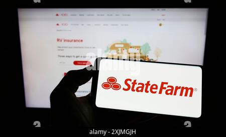 Stuttgart, 16.07.2022: Person, die ein Mobiltelefon hält, mit dem Logo der US State Farm Mutual Automobile Insurance Company vor dem Bildschirm Stockfoto