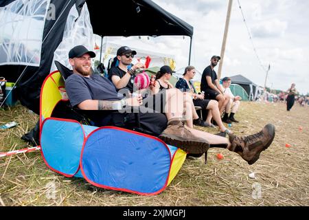 Nordholz, Deutschland. Juli 2024. Festivalbesucher Leon aus Dortmund sitzt mit seinen Freunden auf dem Campingplatz Deichbrand Festival. Das Open-Air-Festival mit rund 60.000 Besuchern findet vom 18. Bis 21. Juli statt. Quelle: Hauke-Christian Dittrich/dpa/Alamy Live News Stockfoto