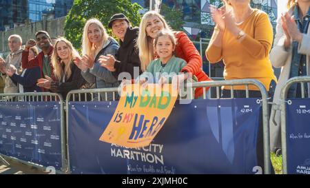 Verschiedene Gruppen von Menschen, die tagsüber einen Marathon in einer Stadt laufen. Unterstützende Familienmitglieder in der Familie: Das kleine Mädchen und ihre Mutter jubeln ihrem Vater im Publikum zu Stockfoto