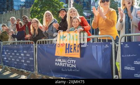 Verschiedene Gruppen von Menschen, die tagsüber einen Marathon in einer Stadt laufen. Unterstützende Familienmitglieder in der Familie: Das kleine Mädchen und ihre Mutter jubeln ihrem Vater im Publikum zu Stockfoto