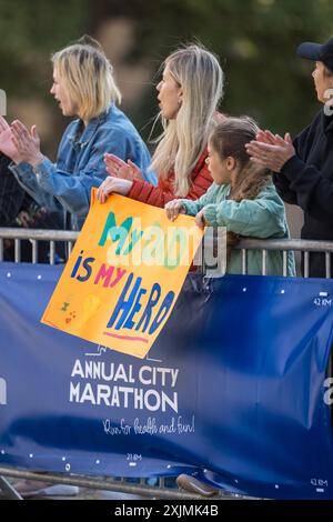 Verschiedene Gruppen von Menschen, die tagsüber einen Marathon in einer Stadt laufen. Unterstützende Familienmitglieder in der Familie: Das kleine Mädchen und ihre Mutter jubeln ihrem Vater im Publikum zu Stockfoto