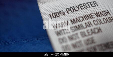 Bekleidungsetikett aus Polyester mit Hinweisen zur Wäschepflege auf blauem Hemdtrikot Stockfoto