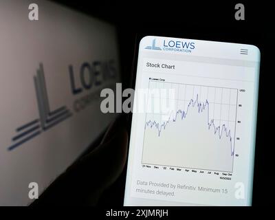 Stuttgart, Deutschland, 10.03.2022: Person, die ein Mobiltelefon hält, mit Webseite des US-amerikanischen Konglomerats Loews Corporation auf dem Bildschirm vor dem Firmenlogo. Fokus Stockfoto
