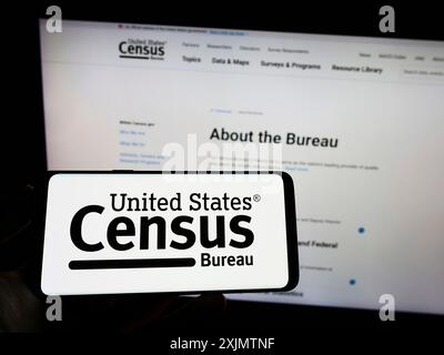 Stuttgart, 23.10.2022: Person, die ein Mobiltelefon mit dem Logo der US-amerikanischen Behörde United States Census Bureau (USCB) auf dem Bildschirm vor der Webseite hält. Stockfoto