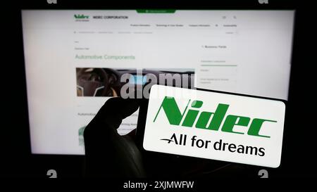 Stuttgart, Deutschland, 12.02.2022: Person, die ein Mobiltelefon mit dem Logo des japanischen Kraftfahrzeugunternehmens Nidec Corporation auf dem Bildschirm vor dem Geschäft hält Stockfoto