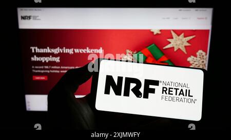 Stuttgart, Deutschland, 12.02.2022: Person, die ein Mobiltelefon hält, mit dem Logo des American Association National Retail Federation (NRF) auf dem Bildschirm vor dem Bildschirm Stockfoto