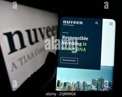 Stuttgart, Deutschland, 12.02.2022: Person, die ein Mobiltelefon hält, mit Website der US-amerikanischen Vermögensverwaltungsgesellschaft Nuveen auf dem Bildschirm vor dem Firmenlogo. Stockfoto