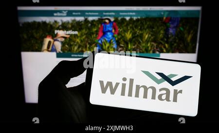 Stuttgart, Deutschland, 12.02.2022: Person, die ein Mobiltelefon mit dem Logo des singapurischen Unternehmens Wilmar International Limited auf dem Bildschirm vor der Webseite hält. Stockfoto