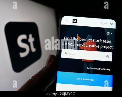 Stuttgart, Deutschland, 12.30.2022: Person, die ein Smartphone hält, mit Website der US-amerikanischen Mikrostock-Agentur Adobe Stock vor dem Firmenlogo auf dem Bildschirm. Fokus Stockfoto