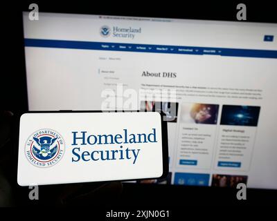 Stuttgart, Deutschland, 01-13-2023: Person, die ein Mobiltelefon mit dem Siegel des US Department of Homeland Security (DHS) auf dem Bildschirm vor der Webseite hält. Fokus Stockfoto