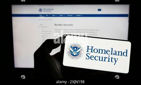 Stuttgart, Deutschland, 01-13-2023: Person, die ein Smartphone mit dem Siegel des US Department of Homeland Security (DHS) auf dem Bildschirm vor der Website hält. Fokus Stockfoto