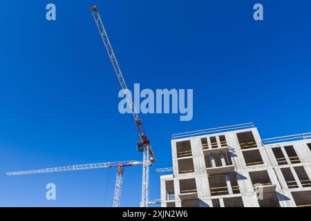 Baukräne und moderne Betonhauskörper mit leeren Fenstern stehen unter blauem Himmel Stockfoto