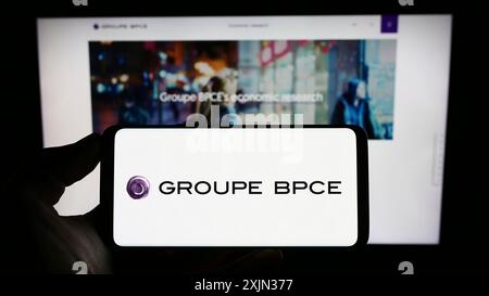 Stuttgart, Deutschland, 13.03.2023: Person, die ein Mobiltelefon mit dem Logo der französischen Bankgesellschaft Groupe BPCE auf dem Bildschirm vor der Webseite des Unternehmens hält. Stockfoto