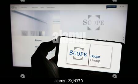 Stuttgart, Deutschland, 13.03.2023: Person mit Mobiltelefon mit Logo der europäischen Fondsbewertungsgesellschaft Scope Group auf dem Bildschirm vor dem Unternehmen Stockfoto