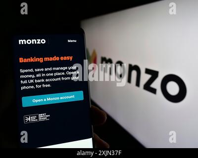 Stuttgart, Deutschland, 13.03.2023: Person, die ein Mobiltelefon hält, mit Webseite des britischen Bankunternehmens Monzo Bank Limited auf dem Bildschirm vor dem Logo. Fokus Stockfoto