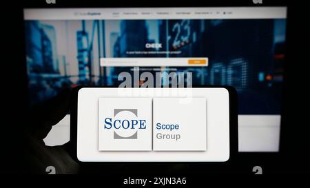 Stuttgart, Deutschland, 13.03.2023: Person, die ein Smartphone mit dem Logo der europäischen Fondsbewertungsgesellschaft Scope Group auf dem Bildschirm vor der Website hält. Fokus Stockfoto