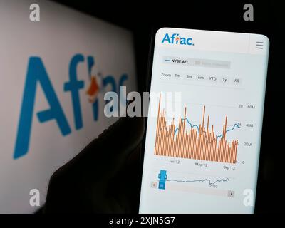 Stuttgart, Deutschland, 26.04.2023: Person mit Smartphone und Webseite der US-Versicherungsgesellschaft Aflac Inc. Auf dem Bildschirm vor dem Firmenlogo. Fokus Stockfoto