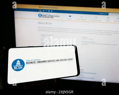 Stuttgart, Deutschland, 28.04.2023: Person, die ein Smartphone mit dem Logo von Business, Consumer Services and Housing Agency auf dem Bildschirm vor der Website hält. Stockfoto