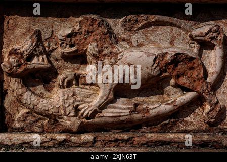 Löwe und Drache aus rotem Porphyr von Veronese. Zerbröckelnder mittelalterlicher Fries am Westportal der Chiesa di Sant’Apollinare in Trient, Trentino-Südtirol, Italien. Stockfoto