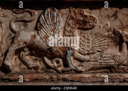 Drache besiegt von mythischen geflügelten Kreaturen, möglicherweise einem gryphon. Mittelalterliche Skulptur aus rotem Porphyr Veronese, Chiesa di Sant’Apollinare in Trient, Trentino-Südtirol, Italien. Es gibt eine offensichtliche Reparatur am Vorderbein des gryphons. Stockfoto