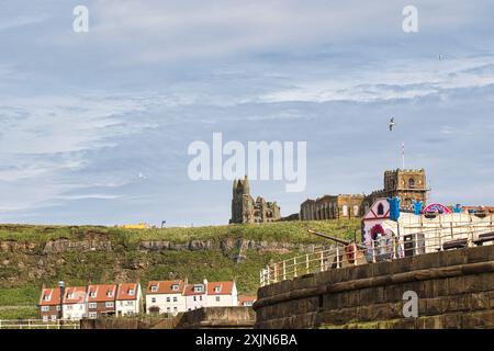 Ein malerischer Blick auf die Ruinen der Whitby Abbey auf einem Hügel mit Häusern und einem Jahrmarkt im Vordergrund unter teilweise bewölktem Himmel. Stockfoto