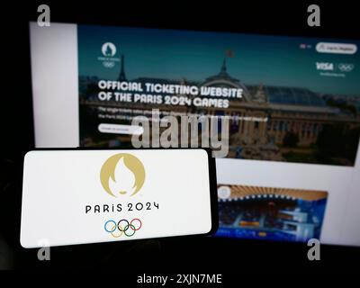 Stuttgart, Deutschland, 19.06.2023: Person mit Handy mit Logo der Olympischen Sommerspiele 2024 in Paris auf dem Bildschirm vor der Webseite. Konzentrieren Sie sich auf das Telefon Stockfoto