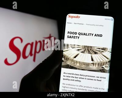 Stuttgart, Deutschland, 18.06.2023: Person, die ein Mobiltelefon hält und die Webseite des kanadischen Molkereiunternehmens Saputo Inc. Vor dem Logo auf dem Bildschirm anzeigt. Konzentrieren Sie sich auf Stockfoto