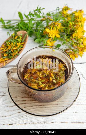 Hypericum perforatum, auch bekannt als Johanniskraut, Johanniskraut oder Johanniskraut Kräutertee in Glas auf weißem Holzbrett. Stockfoto