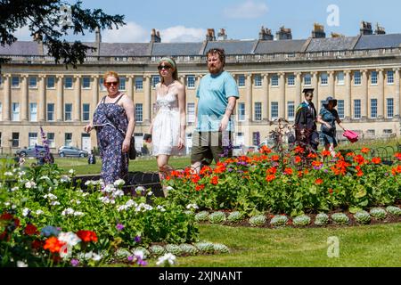 Bath, Großbritannien, 19. Juli 2024. In vielen Teilen Englands und Wales herrschen warme Temperaturen von 31 °C. der weltberühmte Royal Crescent im Hinterland ist zu sehen, wie die Menschen das sehr warme Wetter genießen und an bunten Blumen im Royal Victoria Park vorbeilaufen. Quelle: Lynchpics/Alamy Live News Stockfoto