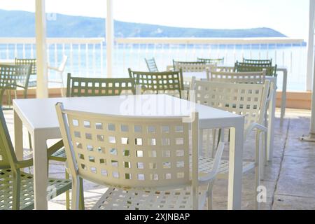 Leere Tische und Stühle eines Straßencafés an der Küste. Am frühen Morgen stehen kostenlose Plätze auf der Terrasse des Cafés zur Verfügung. Stockfoto