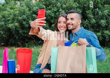 Junge Erwachsene Paare sitzen in der Innenstadt und machen ein Selfie Portait mit ihren Einkaufstaschen. Zwei lächelnde Paare haben Spaß beim Fotografieren, um sie in der Social-Media-Anwendung zu teilen. Hochwertige Fotos Stockfoto