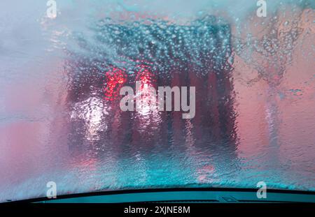 Seifenwasser sprüht über die Windschutzscheibe des Autos, während das Fahrzeug durch die automatische Waschanlage fährt Stockfoto