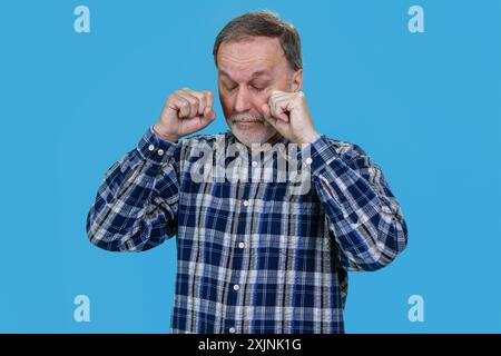 Porträt eines weinenden älteren Mannes, der seine Tränen abwischt. Isoliert auf Blau. Stockfoto