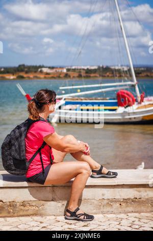 Frau, die sich ausruht und auf der Suche nach einem Boot an der Küste während einer Wanderung im typischen Fischerdorf Alvor in der Algarve, Portugal Stockfoto