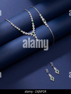 Elegantes Schmuckset mit grünen Edelsteinen und Diamanten auf dunkelblauem Hintergrund. Stockfoto