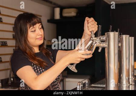 Schöne Barkeeperin, die aus dem Zapfhahn frisches Bier in das Glas im Pub gießt. Stockfoto